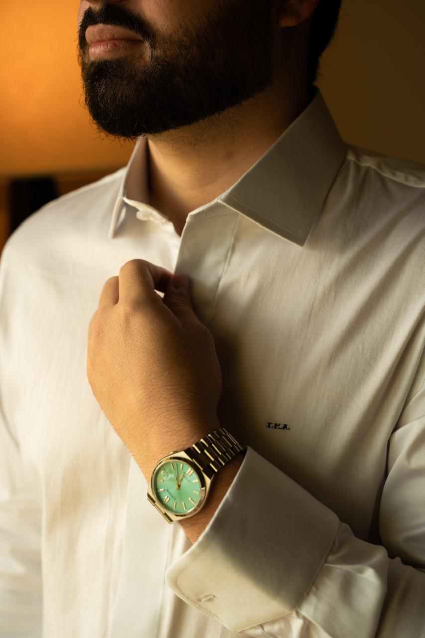Detalhe da camisa branca com monograma bordado e relógio de mostrador verde-água