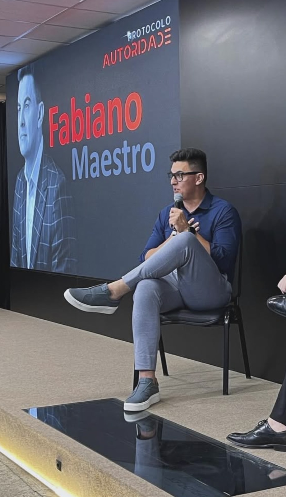 Fabiano Maestro palestrando em evento, com seu nome no telão ao fundo